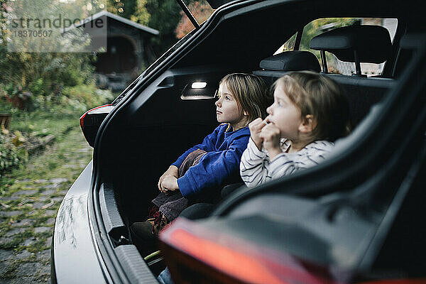 Mädchen  das im Kofferraum eines Elektroautos sitzt und von seiner Schwester träumt