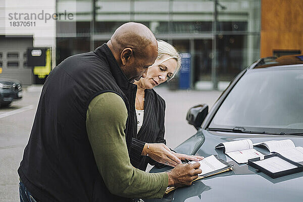 Verkäuferin  die einem männlichen Kunden hilft  während sie in der Nähe des Autos stehend Papierkram erledigt