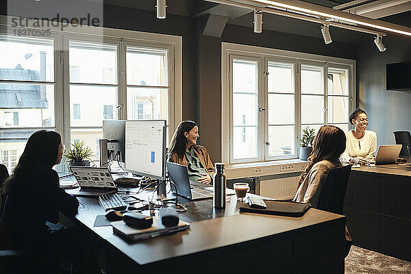 Glückliche Unternehmerinnen  die miteinander kommunizieren  während sie am Schreibtisch im Büro sitzen