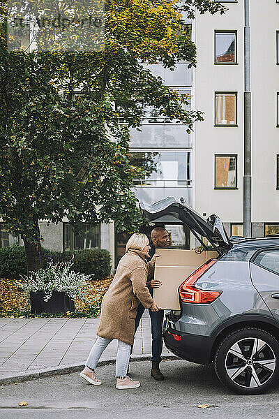 Älteres Paar  das während eines Umzugs gemeinsam Karton in den Kofferraum eines Autos lädt