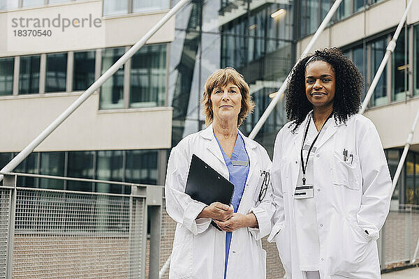 Porträt einer selbstbewussten  multirassischen Ärztin  die vor einem Krankenhaus steht