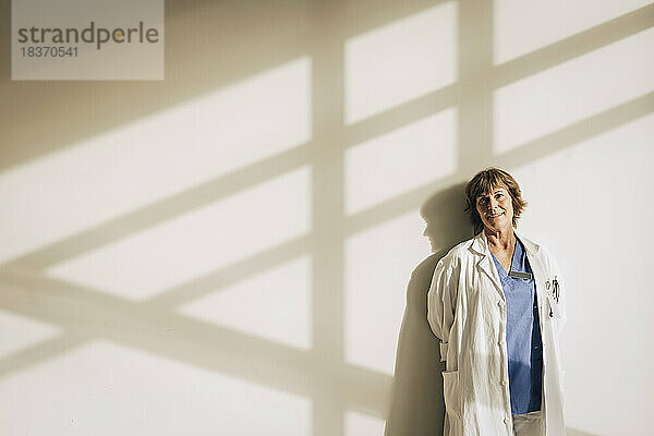 Porträt einer reifen Ärztin  die gegen eine Wand mit Schatten steht