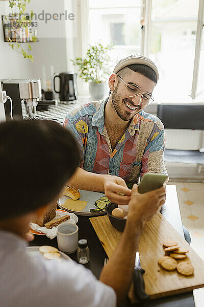 Mann teilt Smartphone mit Freund beim Essen zu Hause