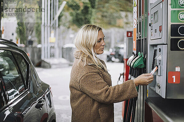 Reife Frau beim Bezahlen mit Kreditkarte an einer Tankstelle