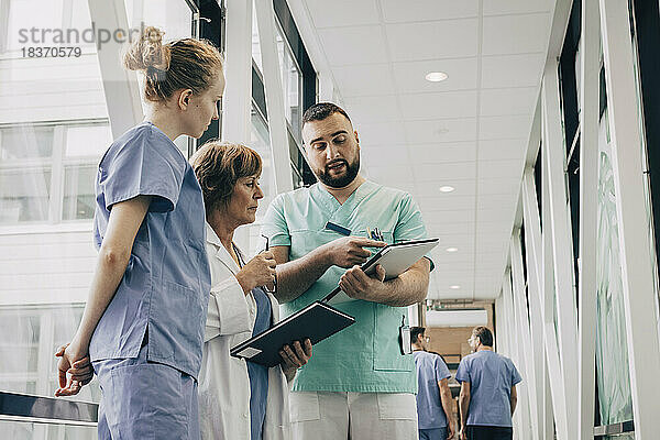 Männlicher Angestellter im Gesundheitswesen erklärt einem Arzt im Krankenhaus das Klemmbrett