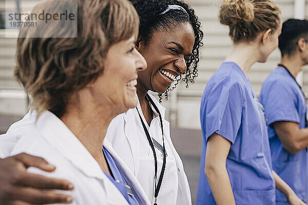 Glückliche Ärztin mit Arm um einen Kollegen vor einem Krankenhaus