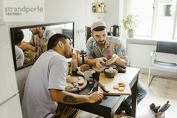 Homosexuelles Paar  das sein Smartphone miteinander teilt  während es zu Hause am Esstisch isst