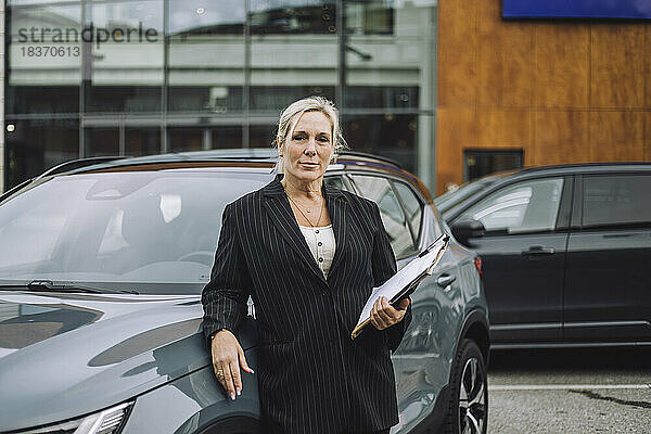Porträt einer selbstbewussten Verkäuferin mit Dokumenten neben einem Auto stehend