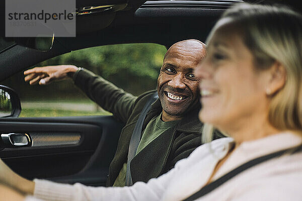 Glücklicher Mann mit Glatze sieht Frau beim Autofahren an