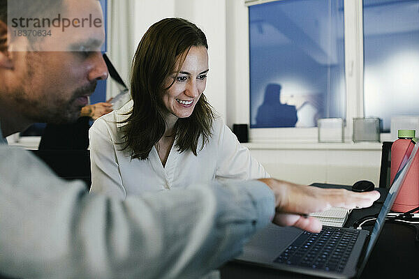 Lächelnde Geschäftsfrau  die mit einem männlichen Kollegen im Büro am Laptop arbeitet