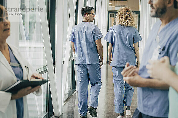 Rückansicht von männlichen und weiblichen Mitarbeitern des Gesundheitswesens  die durch einen Korridor gehen