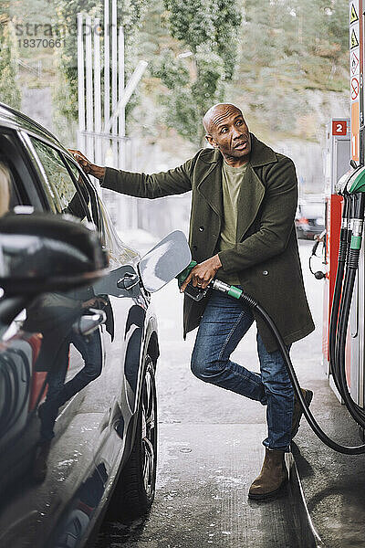 Reifer Mann schaut weg  während er sein Auto an einer Tankstelle auftankt