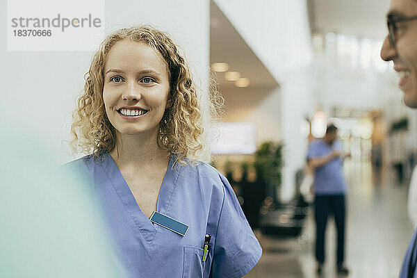 Lächelndes weibliches Gesundheitspersonal mit Kollegen im Krankenhaus