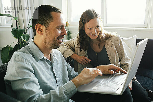 Glückliche Geschäftsleute  die im Büro sitzend gemeinsam an einem Laptop arbeiten