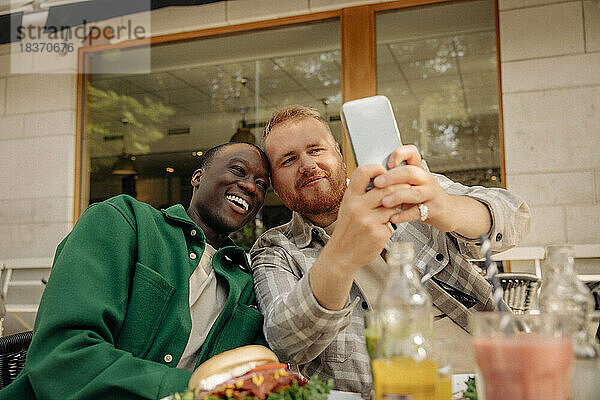 Lächelnde männliche Freunde machen ein Selfie mit ihrem Smartphone in einem Straßencafé