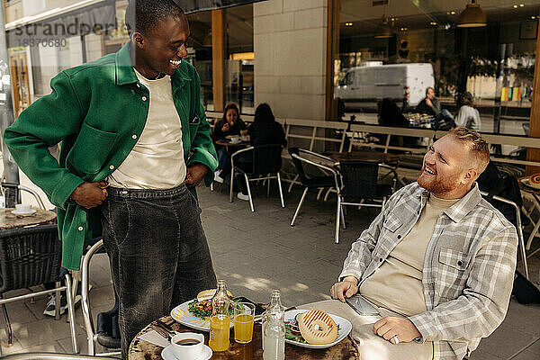 Fröhliche multirassische männliche Freunde  die sich in einem Straßencafé unterhalten