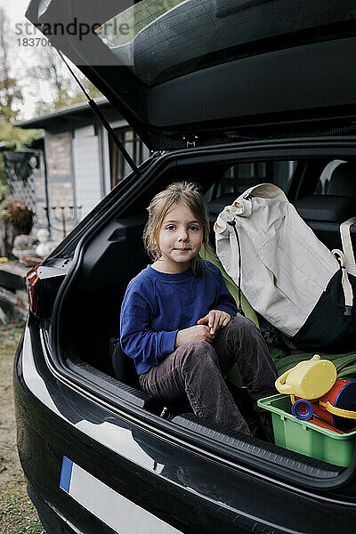 Porträt eines im Kofferraum eines Elektroautos sitzenden Mädchens