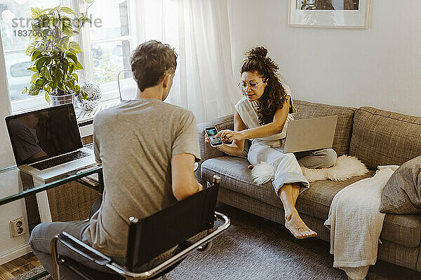 Frau sitzt auf dem Sofa und teilt ihr Smartphone mit ihrem Freund zu Hause