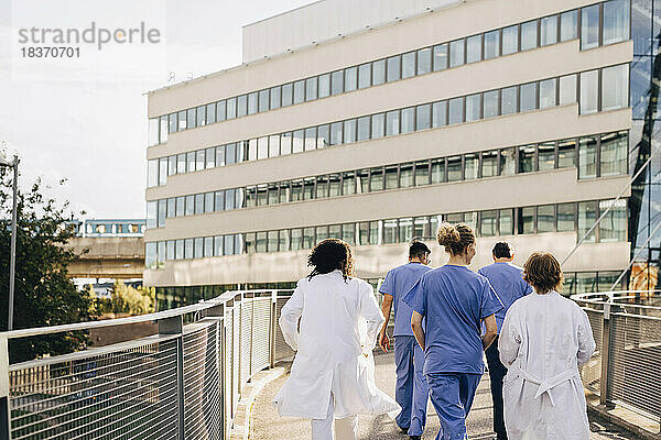Männliches und weibliches Gesundheitspersonal auf einer Brücke  die zum Krankenhaus führt