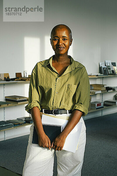 Porträt einer zuversichtlich lächelnden Geschäftsfrau  die ein Dokument hält  während sie im Büro steht