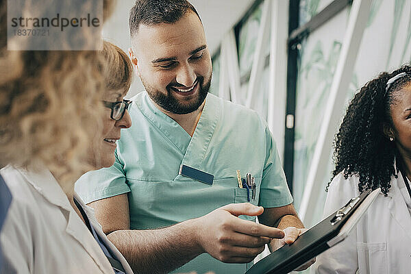 Lächelnde männliche Pflegekraft  die mit einem Arzt über einem Klemmbrett im Krankenhaus diskutiert