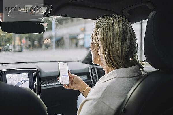Reife Frau  die ein Smartphone benutzt  während sie auf dem Beifahrersitz sitzt