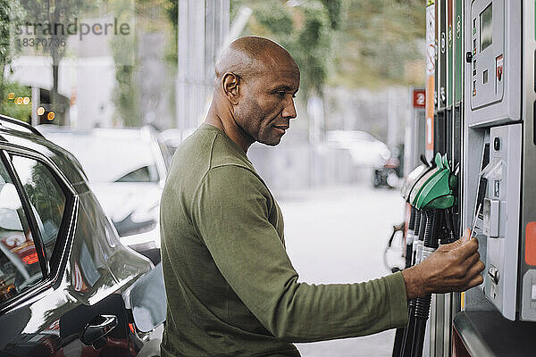 Seitenansicht eines reifen Mannes beim Bezahlen mit Kreditkarte an einer Tankstelle