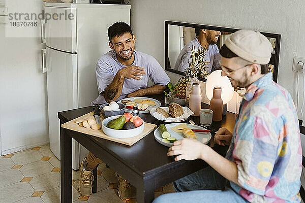 Glückliches homosexuelles Paar  das Früchte isst  während es am Esstisch in der Küche sitzt