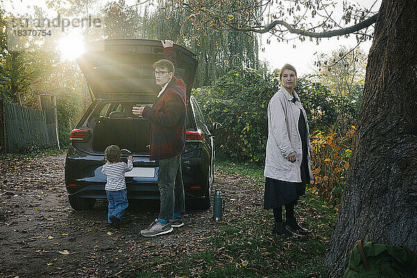 Vater und Mutter mit Tochter stehen an einem sonnigen Tag in der Nähe eines Elektroautos