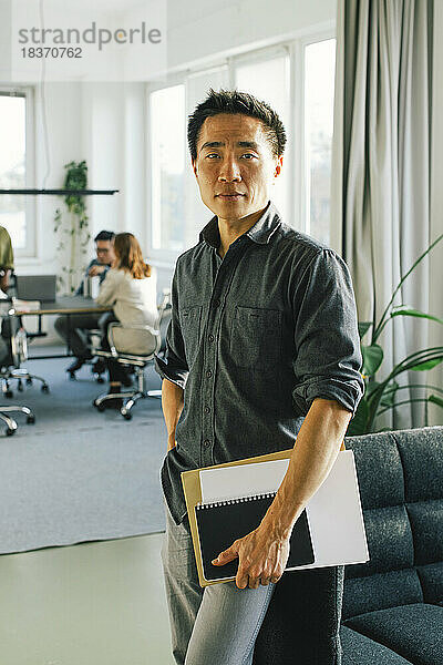 Porträt eines selbstbewussten Geschäftsmannes  der ein Dokument hält  während er im Büro steht