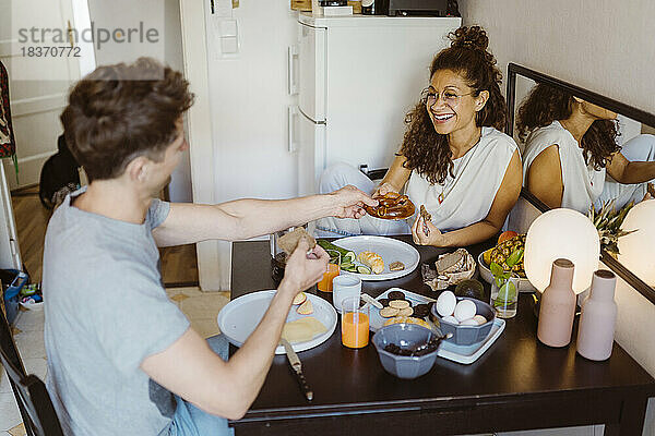Glückliches Paar  das sich am Esstisch zu Hause das Essen teilt