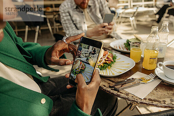 Mann fotografiert Essen auf dem Tisch mit seinem Smartphone in einem Straßencafé