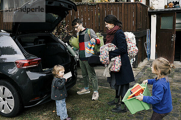 Eltern mit Kindern beim Einladen von Gepäck in den Kofferraum eines Elektroautos im Hinterhof