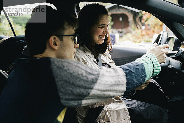 Mann hält Lenkrad  während er einer Frau im Auto sitzend das Fahren beibringt