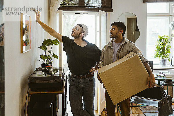 Mann hält Karton  während er mit seinem Freund spricht und ein Gemälde an der Wand betrachtet