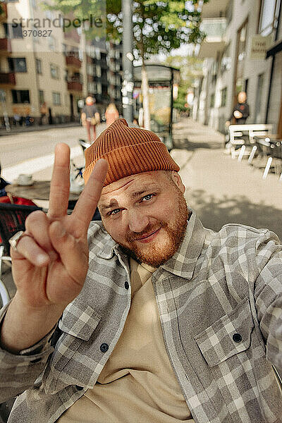 Porträt eines lächelnden Mannes mit Friedenszeichen bei einem Selfie
