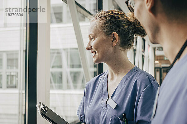 Lächelnde Krankenschwester schaut durch ein Fenster im Krankenhaus