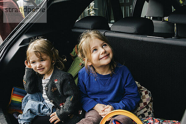 Lächelnde Mädchen sitzen zusammen im Kofferraum eines Elektroautos