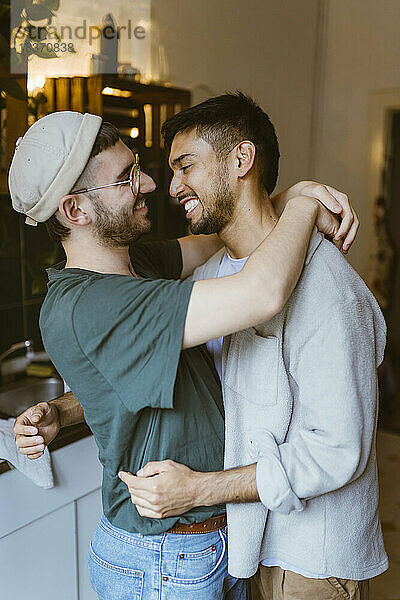 Seitenansicht eines glücklichen schwulen Paares  das sich in der Küche zu Hause umarmt