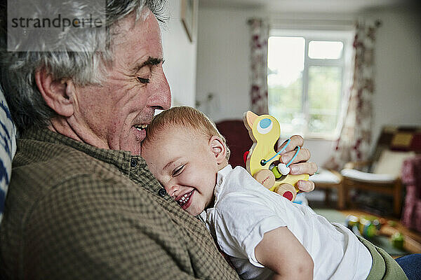 Nahaufnahme eines lachenden Kleinkindes in den Armen seines Großvaters