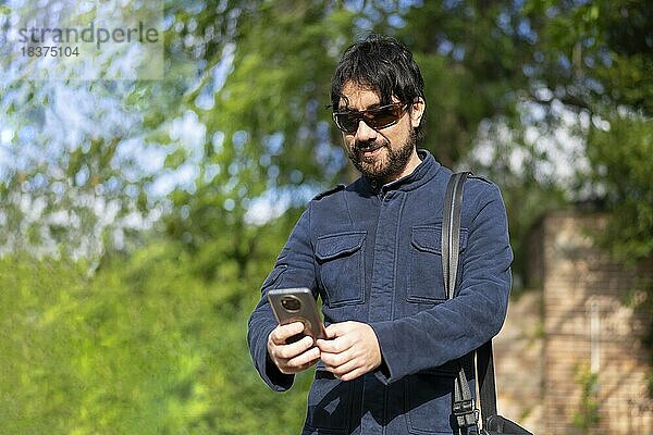 Glücklicher junger gutaussehender hispanischer Hipster Mann  der im Park telefoniert