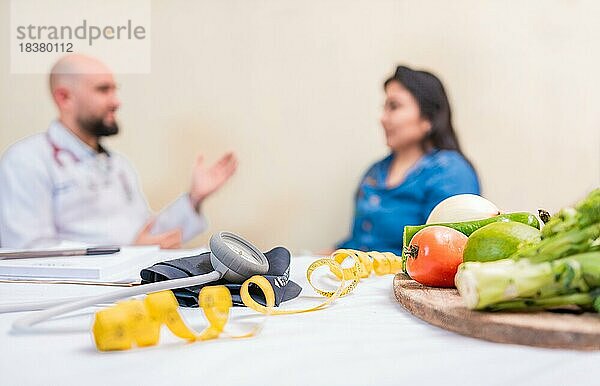 Ernährungsberater Männchen mit Patientin im Büro. Ernährungsberater im Gespräch mit Patientin mit Fokus auf die Früchte im Vordergrund. Konzept der Ernährungsberaterin  die eine Kundin berät