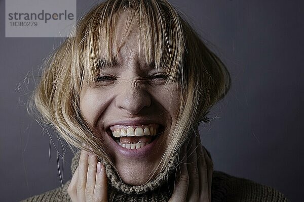 Junge Frau mit Rollkragenpullover und langem Haar lacht in Kamera  Portrait  Studioaufnahme