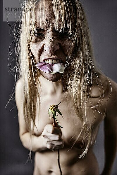 Junge  nackte Frau isst die Blütenblätter einer Rose und schaut aggressiv in die Kamera  Portrait  Studioaufnahme  Köln  Nordrhein-Westfalen  Deutschland  Europa