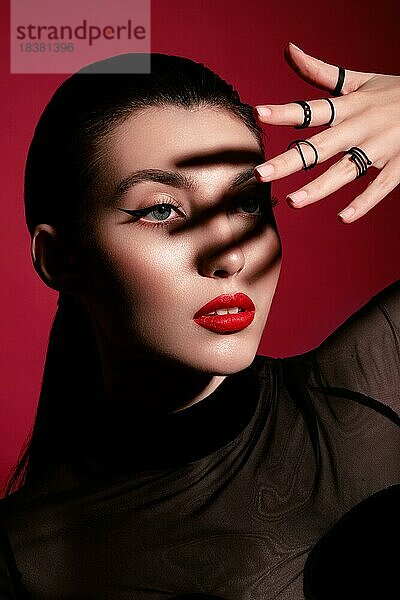 Schöne Frau in schwarzer Kleidung  klassischem Makeup und roten Lippen posiert im Studio auf einem roten Hintergrund. Schönheit Gesicht