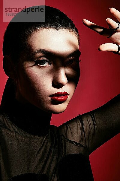 Schöne Frau in schwarzer Kleidung  klassischem Makeup und roten Lippen posiert im Studio auf einem roten Hintergrund. Schönheit Gesicht