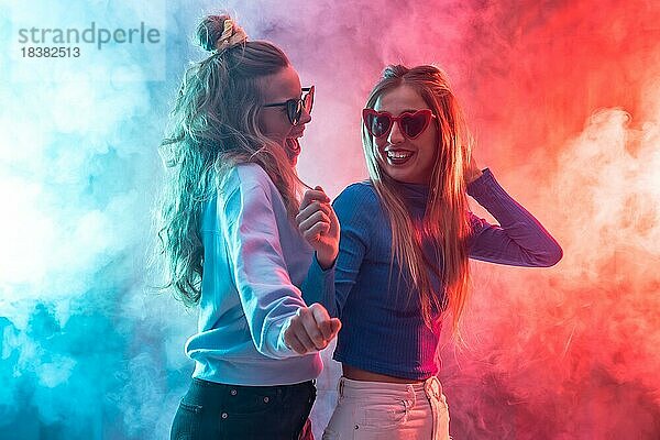 Zwei junge blonde kaukasische Frauen tanzen in einem Nachtclub  tanzen und Spaß haben auf einer Party  rot und blau geführter Rauch