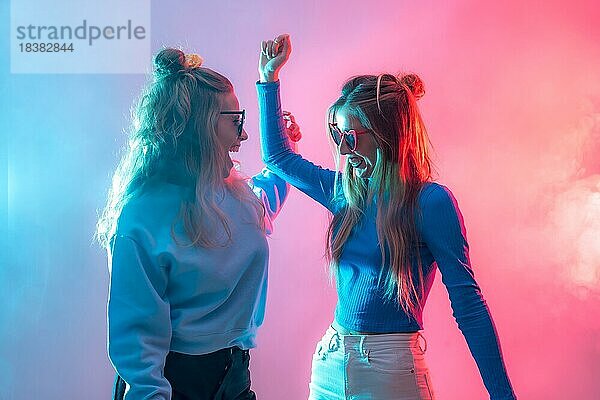Zwei junge blonde kaukasische Frauen tanzen in einem Nachtclub  tanzen und Spaß haben  rot und blau geführter Rauch