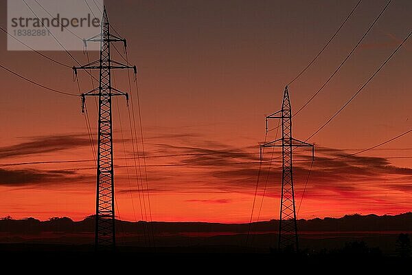 Silhouette von Hochspannungsleitungen und Sendemasten durch das Mährische Feld bei Sonnenaufgang