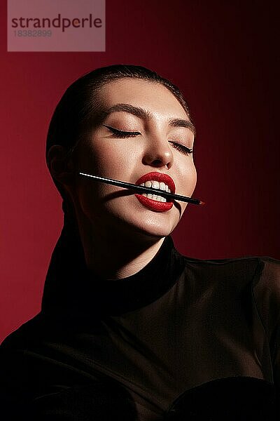 Schöne Frau in schwarzer Kleidung  klassischem Makeup und roten Lippen posiert im Studio auf einem roten Hintergrund. Schönheit Gesicht